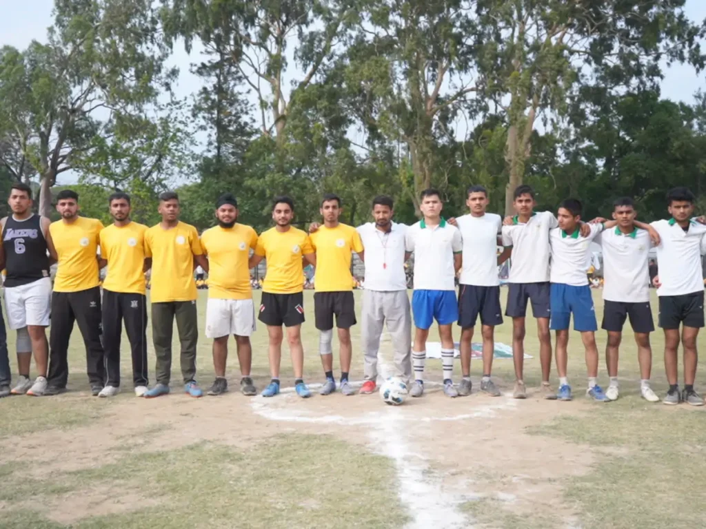 Group of students standing in a line on a sports field with a football placed in front, preparing for a game.